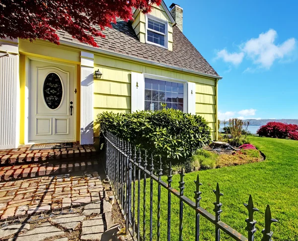 Gele kleine huis met uitzicht op water en rode esdoorn. — Stockfoto
