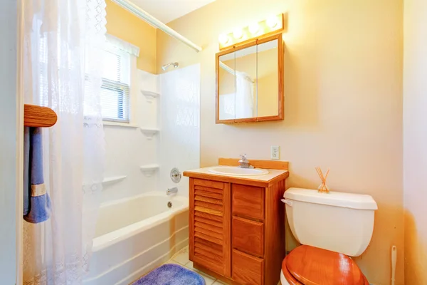 Small simple old bathroom with blue rug and wood cabinet. — Stock Photo, Image