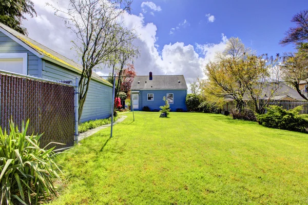 Задний двор с маленьким синим домом и ярко-зеленой весенней травой . — стоковое фото