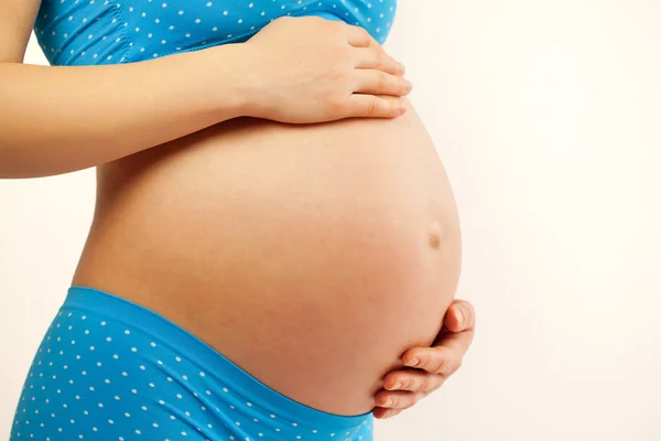 Ung kvinna som håller gravid mage i händerna. — Stockfoto