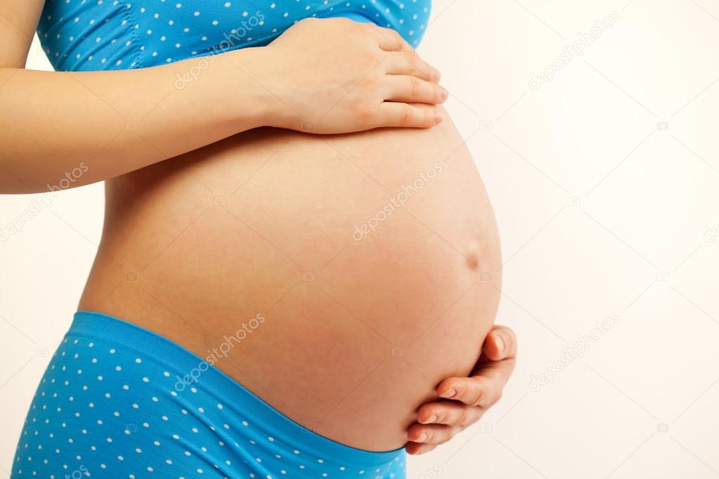 Young woman holding pregnant belly in hands.