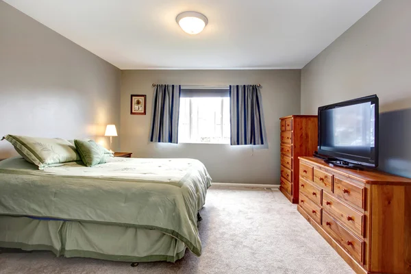 Large grey bedroom with dresser, tv and blue curtains. — Stock Photo, Image