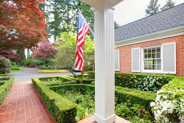 Amerikanisches altes Backsteinhaus mit Flagge und klassischem Garten. — Stockfoto