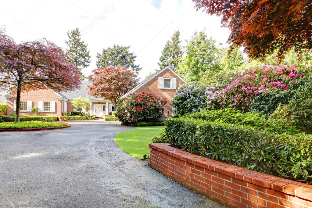 Brick red house with English garden and white window shutters and driveway.