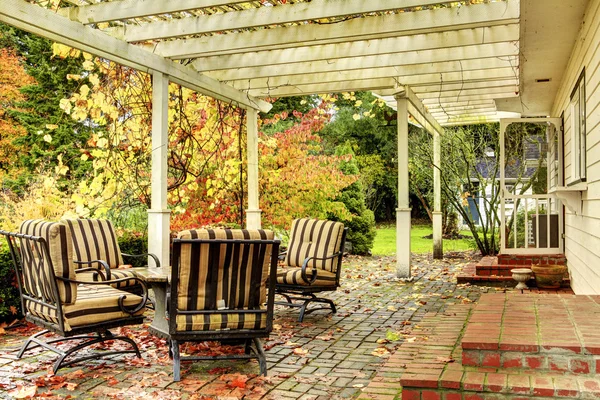 Achterzijde van het witte huis met fall bomen en stoelen. — Stockfoto