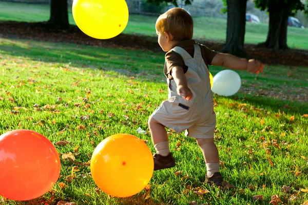 Niño feliz está jugando con globos en el parque durante el atardecer —  Fotos de Stock