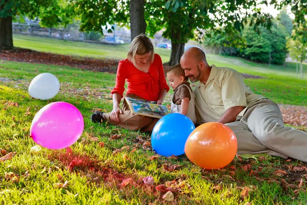 Los padres y el bebé están leyendo en el parque al atardecer. . —  Fotos de Stock