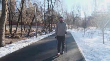 Sakallı adam kış parkında İskandinav yürüyüşü yapıyor. Spor salonu ve açık havada sağlıklı bir yaşam tarzı. Motivasyon ve ilham verici kış manzarası.