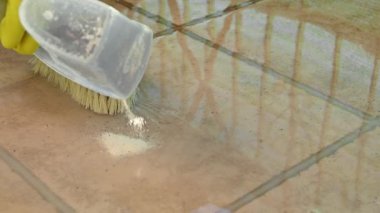 Sarı lastik eldivenli bir insan zemin karolarını fırçalıyor, ağır çekimde