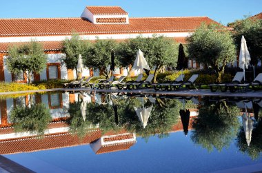 Yüzme havuzu şemsiyeleri ve etrafındaki binaları yansıtıyor.