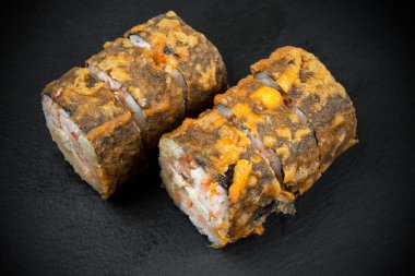 Siyah taş masa zemininde tempura ile pişirilmiş suşi ruloları. Fırınlanmış suşi böreği izole edilmiş. Geleneksel Japon yemekleri ve lezzetli suşi parçaları.