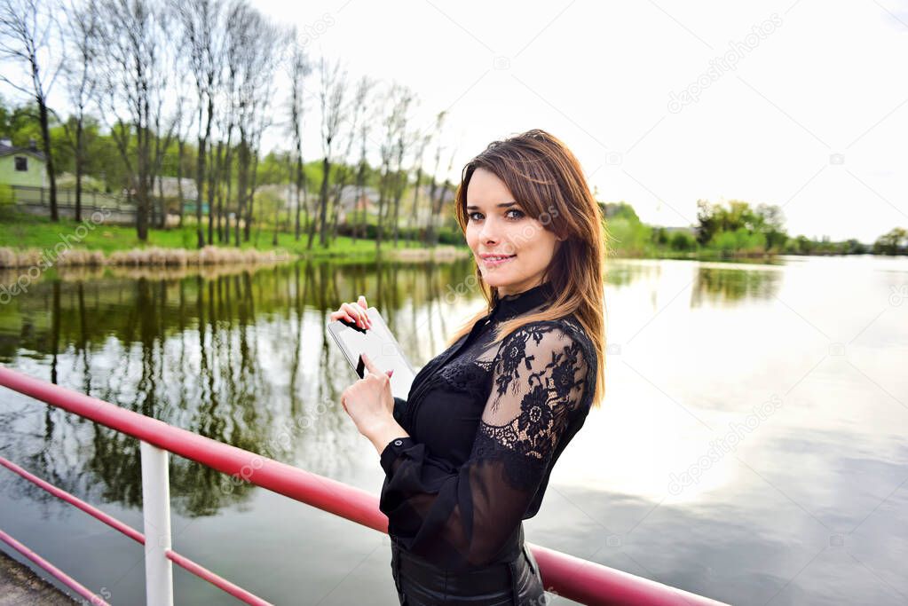 smiling woman holding tablet near lake