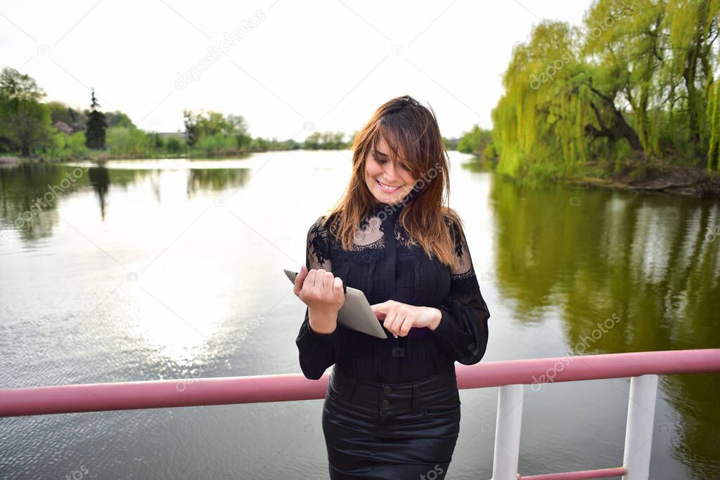 smiling woman looking at the tablet on the background of the lake