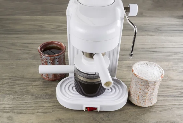 De zwarte en slagroom koffie druppelen op tafel met espresso maker — Stockfoto