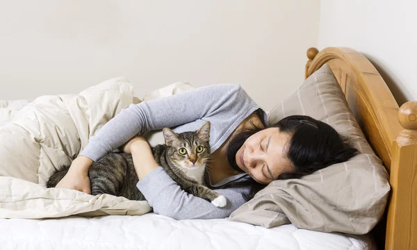 Mujer madura sosteniendo gato mientras está acostado en la cama — Foto de Stock