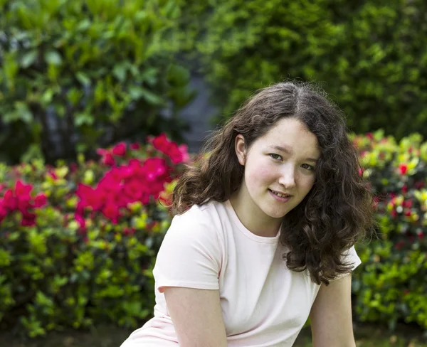 Giovane ragazza seduta all'aperto di fronte a fiori stagionali — Foto Stock