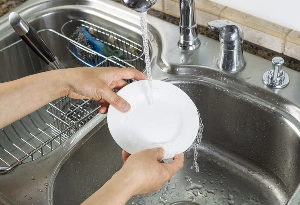 Woman hands washing dinner plate in kitchen sink — Stock Photo, Image