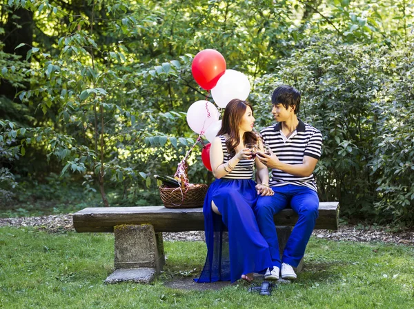 Jeunes amoureux partageant du vin rouge assis sur un banc de bois rond en plein air — Photo