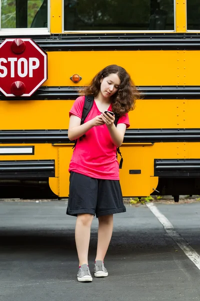 Chica caminando lejos de autobús escolar, mientras que los mensajes de texto en su teléfono —  Fotos de Stock
