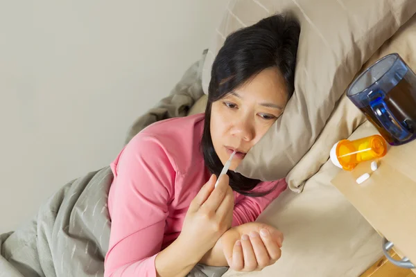Reife Frau benutzt Thermometer, während sie krank im Bett liegt — Stockfoto