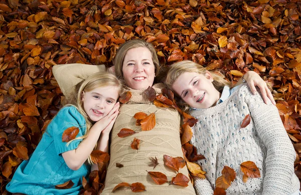 Mom and her daughters lying on a bed of leaves during the fall s — Stock Photo, Image