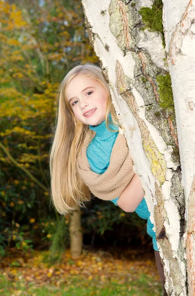 Jovem garota espreitando de trás da árvore durante o dia agradável no outono — Fotografia de Stock