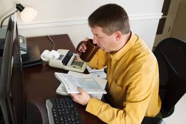 Dojrzały człowiek działa na jego podatek dochodowy, podczas gdy w biurze — Zdjęcie stockowe
