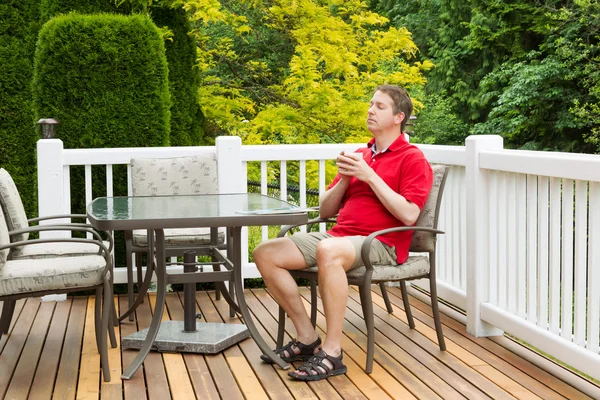 Mature man resting in chair on outdoor patio with cup of coffee