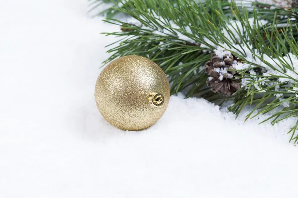 Adorno de Navidad de oro en la nieve con rama de abeto —  Fotos de Stock