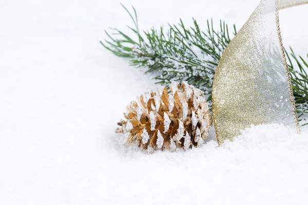Cono de pino dorado con cinta y rama de abeto en la nieve —  Fotos de Stock