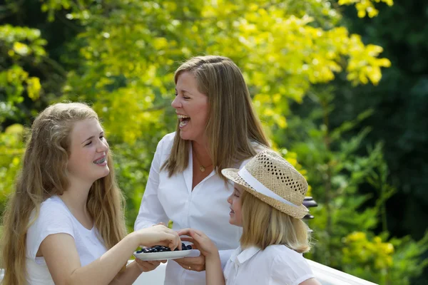 Mother and daughters laughing while eating berries outside — Stock Photo, Image