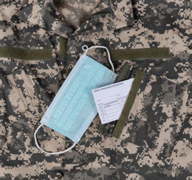 Üzerinde Covid 19 aşı kartı ve cebinde kişisel maske olan bir askeri üniforma. 