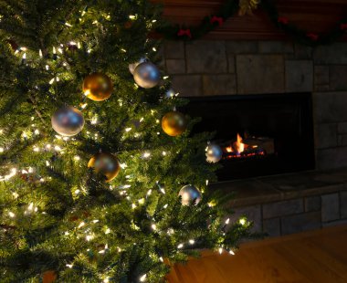 Gümüş ve altın renkli süslemelerle süslenmiş parlak Noel ağacı artı tatil sezonu için arka planda parlayan şömine.  