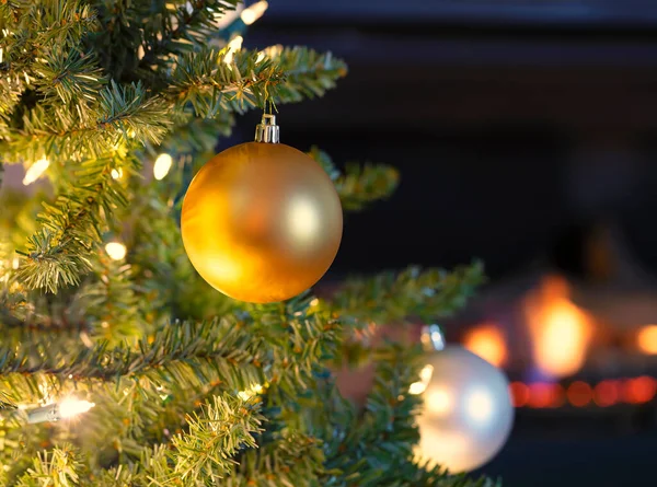 ホリデーシーズンのために背景に輝く暖炉と明るいクリスマスツリーからぶら下がっ単一の金のボールの装飾 — ストック写真