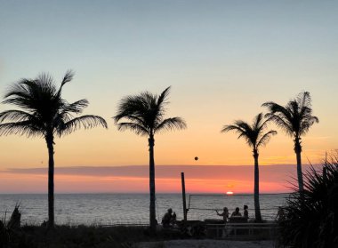 Voleybol oyuncuları, arka planda okyanus ve günbatımı olan plajda siluet oluşturdular. 