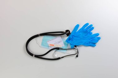 Covid 19 için hızlı test cihazı negatif test sonucu, kişisel maske, steteskop, lateks eldiven ve aşı kartını beyaz arka planda gösteriyor.