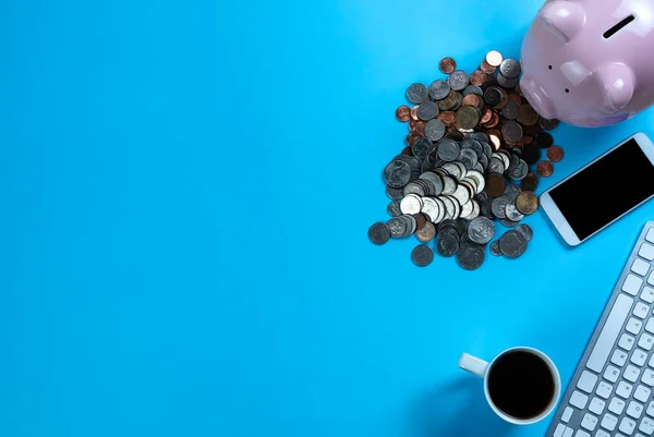 コンピュータ技術と青の机の上に貯蓄や投資の概念のためのコインの山ピンクの貯金箱 — ストック写真