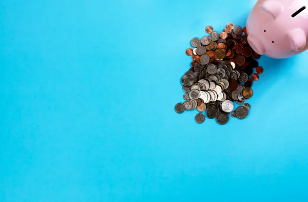 粉红储蓄罐 为节省开支或投资而在蓝桌顶部堆放大量硬币 — 图库照片