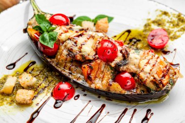 Restoranda yemek. Peynirle doldurulmuş ızgara patlıcan, domates ve pesto soslu sebze, doğranmış fesleğen serpiştirilmiş.