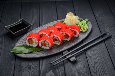 Siyah arka planda geleneksel lezzetli suşi rulosu. Pilavlı suşi, nori, krem peynir, tobiko havyarı, avokado. Suşi menüsü. Japon mutfağı, restoran. Asya yemekleri