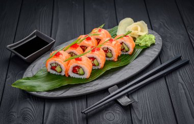 Siyah arka planda geleneksel lezzetli suşi rulosu. Pilavlı suşi, nori, krem peynir, tobiko havyarı, avokado. Suşi menüsü. Japon mutfağı, restoran. Asya yemekleri