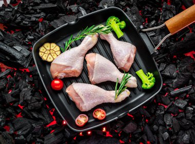 Tavada çiğ tavuk budu, sebze ve baharatla ızgarada duruyor.