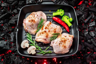 Tavada çiğ tavuk butları ve sebze ve baharatlar ızgarada duruyor. Organik et