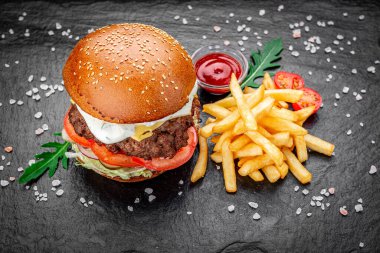 Siyah arka planda kızarmış patatesli bir Amerikan hamburgeri..