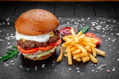 Siyah arka planda kızarmış patatesli bir Amerikan hamburgeri..