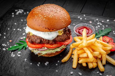 Siyah arka planda kızarmış patatesli bir Amerikan hamburgeri..
