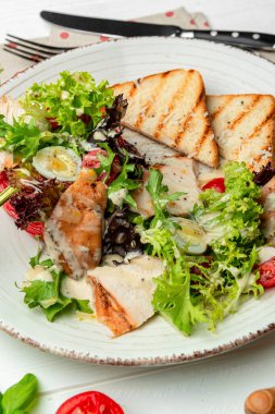 Peynirli ve çıtır çıtır tavuklu Sezar salatası. Karanlık bir arka planda