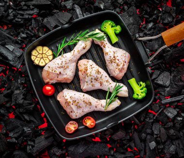 Tavada çiğ tavuk budu, sebze ve baharatla ızgarada duruyor.