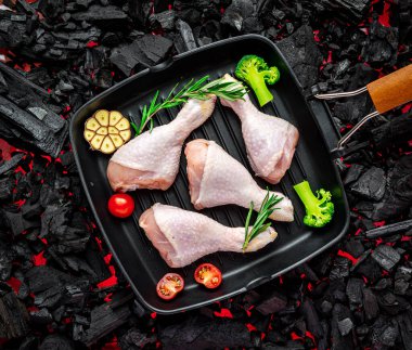 Tavada çiğ tavuk budu, sebze ve baharatla ızgarada duruyor.