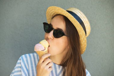 Hasır şapkalı kız dondurma yiyor Gri duvarın yanında
